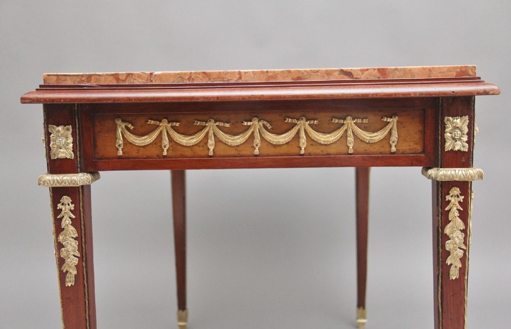 A 19th-century French mahogany centre table featuring a pink marble top, slender tapered legs, and decorative gilt-bronze mounts with swags and cherub relief. View VII