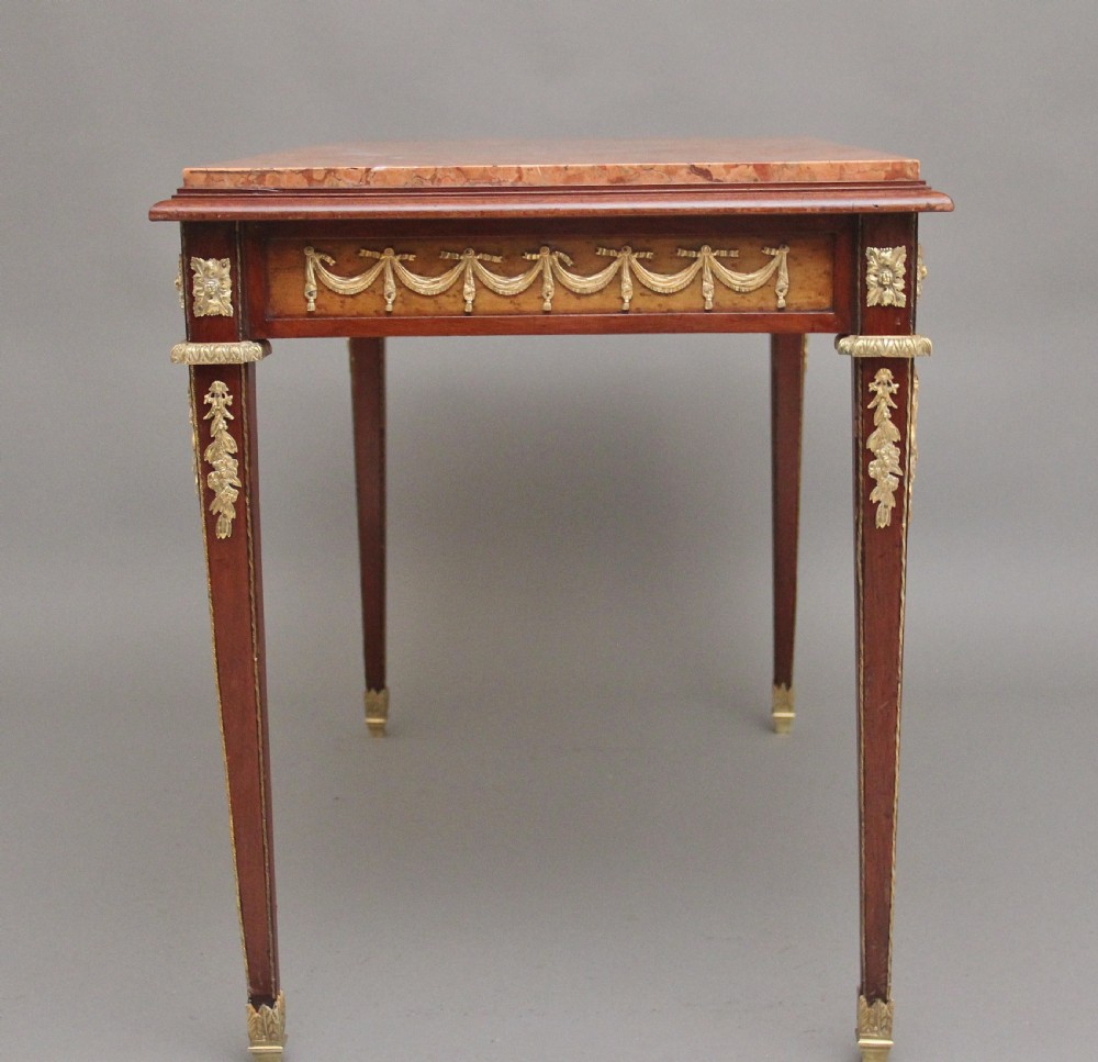 A 19th-century French mahogany centre table featuring a pink marble top, slender tapered legs, and decorative gilt-bronze mounts with swags and cherub relief. View VIII