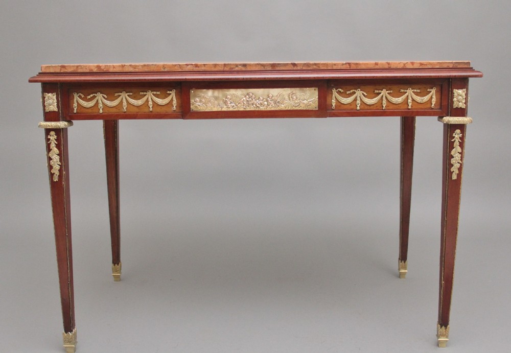 A 19th-century French mahogany centre table featuring a pink marble top, slender tapered legs, and decorative gilt-bronze mounts with swags and cherub relief. View IX