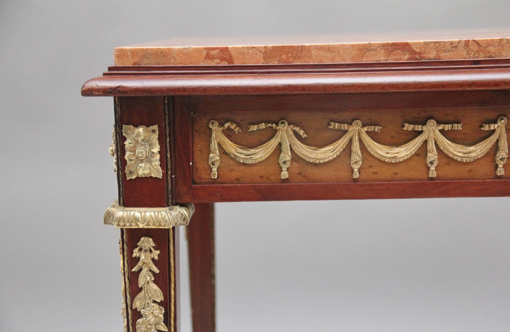 A 19th-century French mahogany centre table featuring a pink marble top, slender tapered legs, and decorative gilt-bronze mounts with swags and cherub relief. View XI