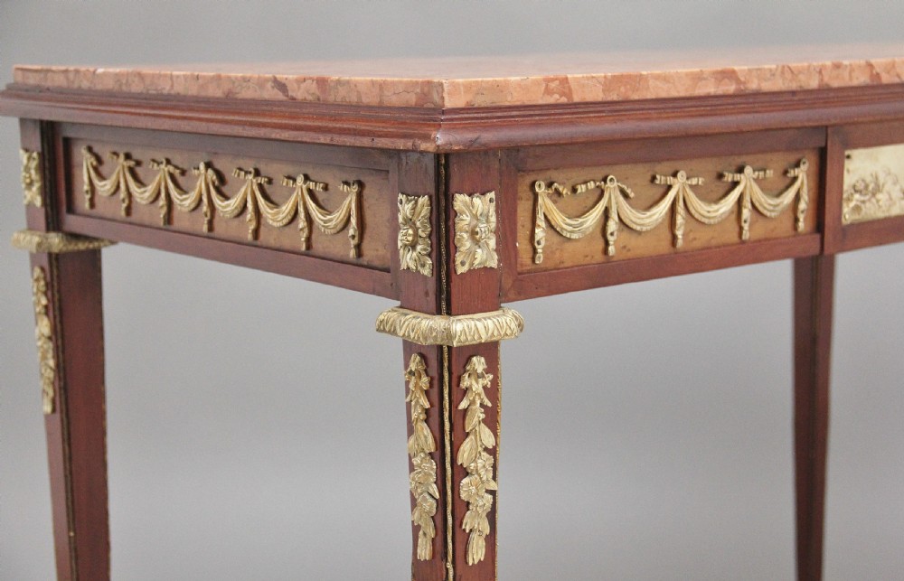 A 19th-century French mahogany centre table featuring a pink marble top, slender tapered legs, and decorative gilt-bronze mounts with swags and cherub relief. View XIV