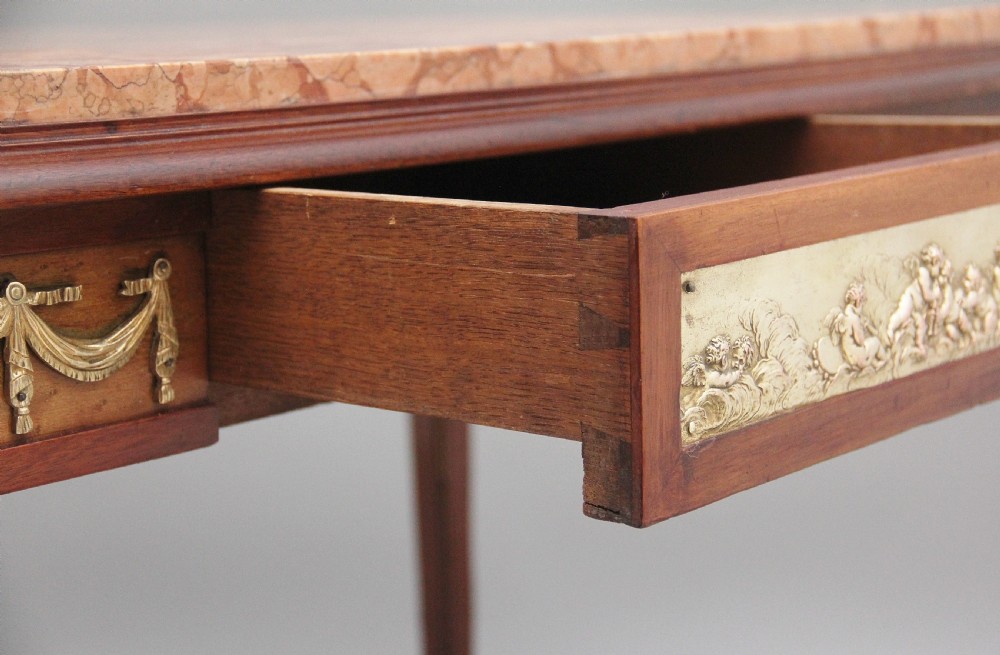 A 19th-century French mahogany centre table featuring a pink marble top, slender tapered legs, and decorative gilt-bronze mounts with swags and cherub relief. View XV