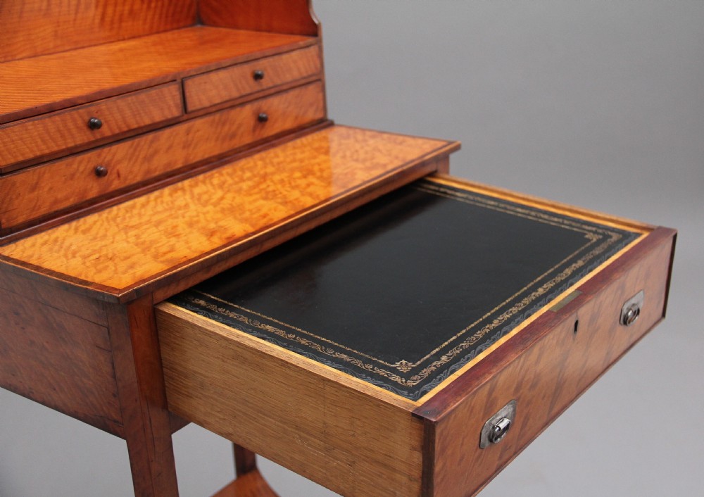 A 19th-century satinwood ladies writing table featuring a raised gallery back with small drawers, a single frieze drawer, square tapered legs, and a curved lower shelf. View IX