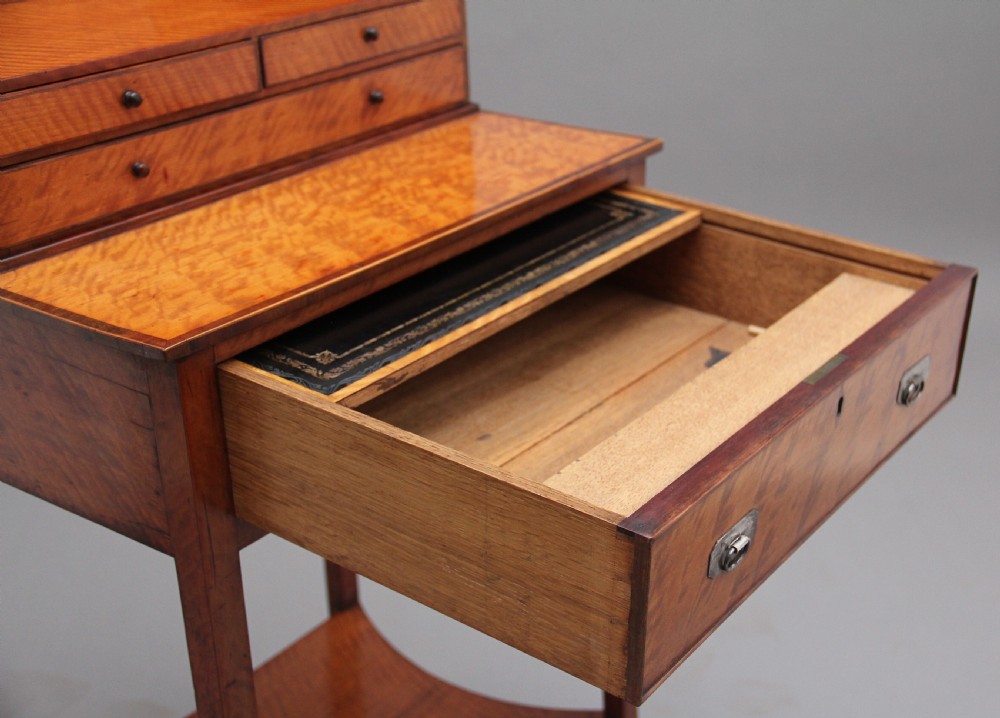 A 19th-century satinwood ladies writing table featuring a raised gallery back with small drawers, a single frieze drawer, square tapered legs, and a curved lower shelf. View X
