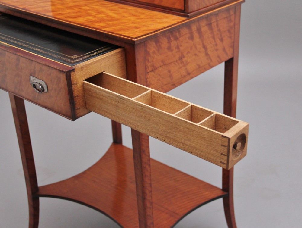 A 19th-century satinwood ladies writing table featuring a raised gallery back with small drawers, a single frieze drawer, square tapered legs, and a curved lower shelf. View XI