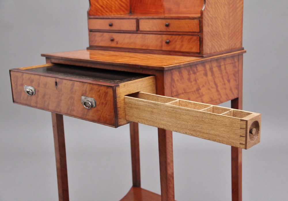 A 19th-century satinwood ladies writing table featuring a raised gallery back with small drawers, a single frieze drawer, square tapered legs, and a curved lower shelf. View XV