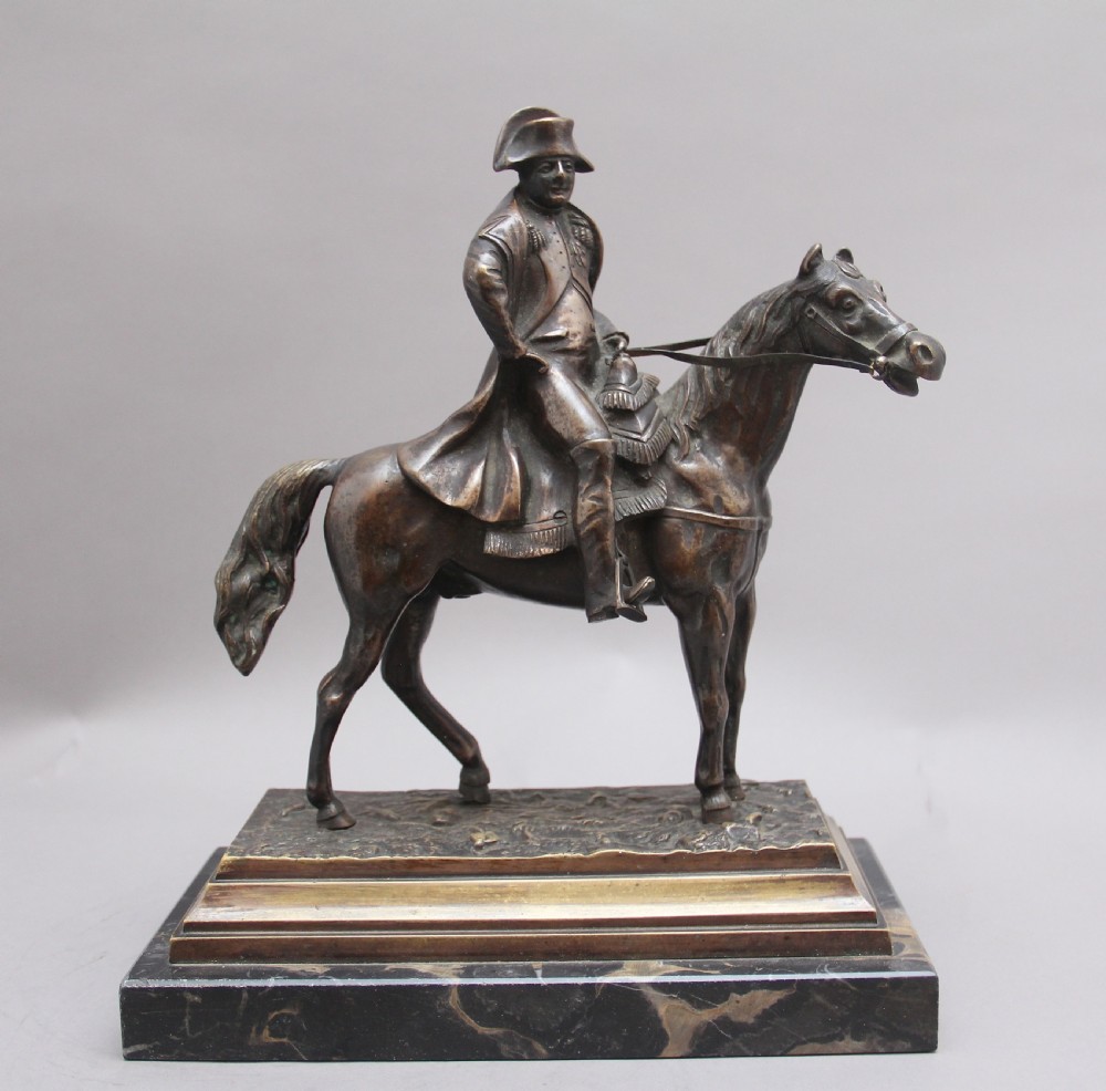 A dark bronze equestrian sculpture depicting Napoleon Bonaparte on horseback mounted on a stepped brass and black marble plinth. View II