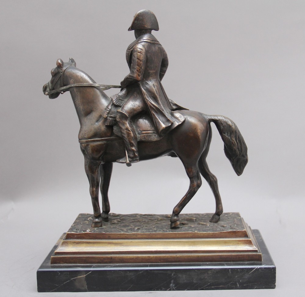 A dark bronze equestrian sculpture depicting Napoleon Bonaparte on horseback mounted on a stepped brass and black marble plinth. View V