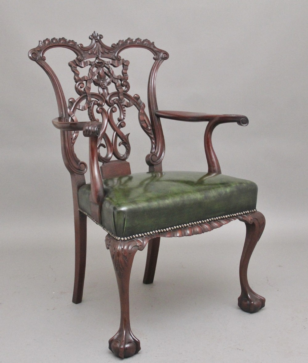 An early 20th-century Chippendale style mahogany armchair featuring a detailed pierced back splat, green leather upholstered seat with brass studding, curved armrests, and cabriole front legs terminating in claw and ball feet.