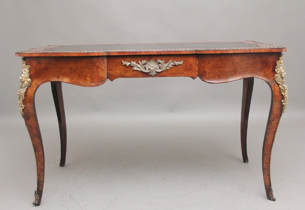 A 19th-century burr walnut bureau plat writing table with decorative gilt-bronze mounts, cabriole legs, and a dark leather inset top.