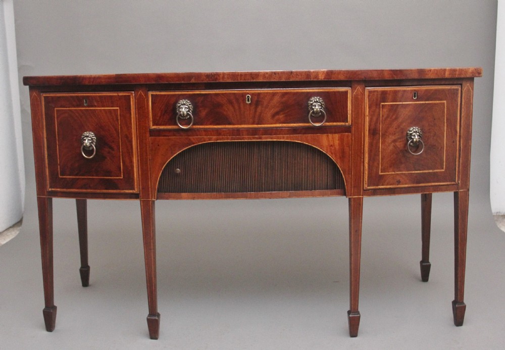 An early nineteenth-century mahogany bowfront sideboard with line inlay, central arch detail, brass lion mask ring handles, and tapered square legs.