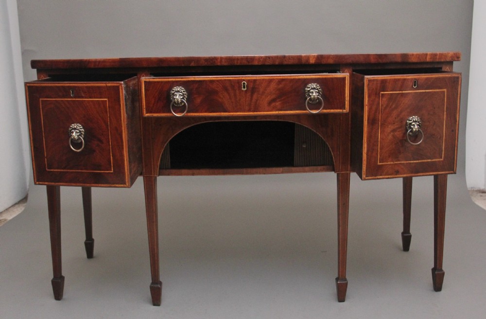 An early nineteenth-century mahogany bowfront sideboard with line inlay, central arch detail, brass lion mask ring handles, and tapered square legs. View II