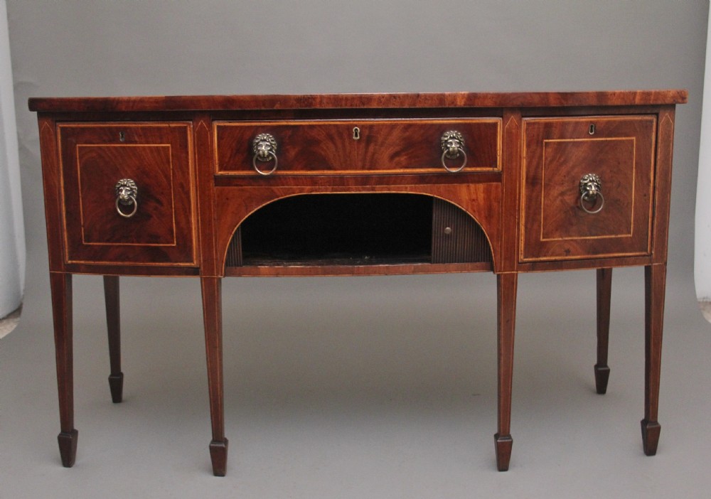 An early nineteenth-century mahogany bowfront sideboard with line inlay, central arch detail, brass lion mask ring handles, and tapered square legs. View III