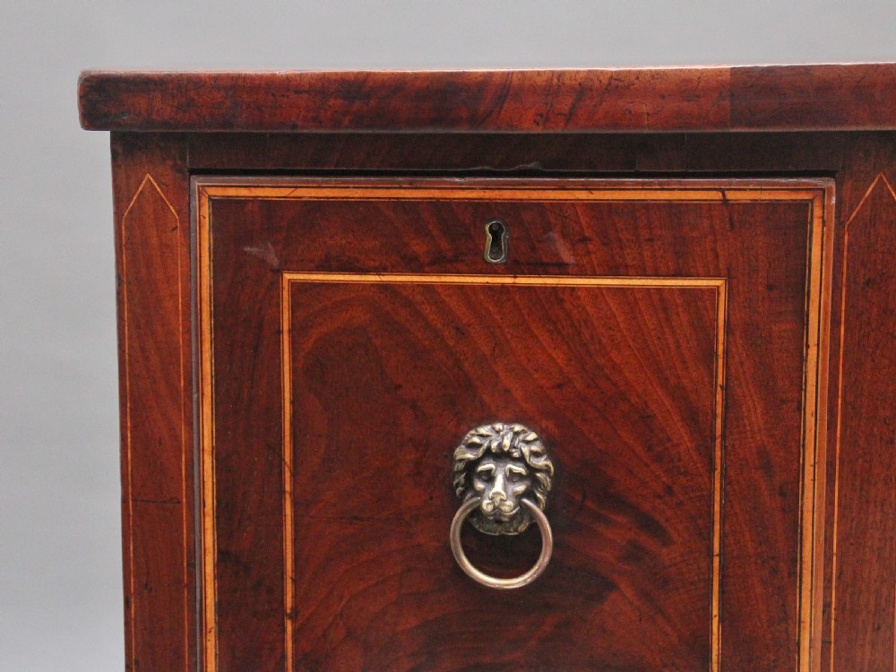 An early nineteenth-century mahogany bowfront sideboard with line inlay, central arch detail, brass lion mask ring handles, and tapered square legs. View V