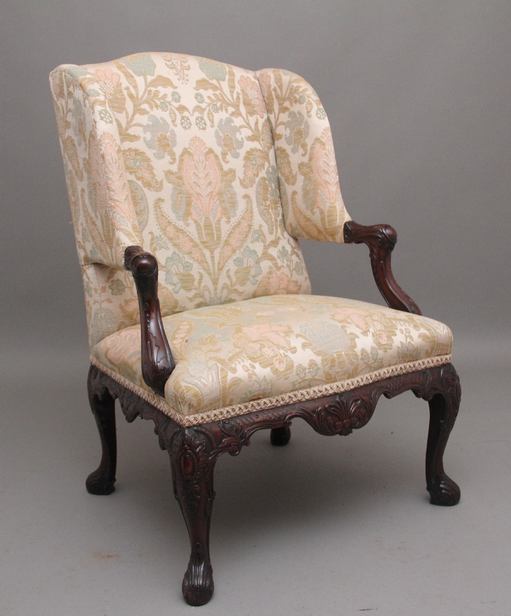 A 19th-century mahogany wingback armchair featuring carved cabriole legs, claw-and-ball feet, and patterned cream damask upholstery.