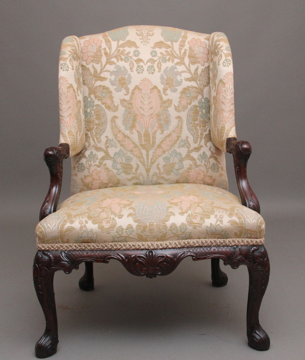 A 19th-century mahogany wingback armchair featuring carved cabriole legs, claw-and-ball feet, and patterned cream damask upholstery. View V
