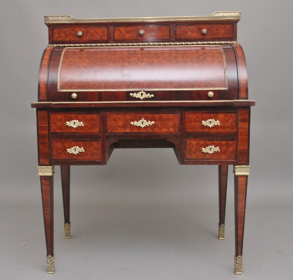 A 19th-century French kingwood cylinder desk featuring parquetry veneering, gilt-brass mounts, tapered square legs, and a curved roll-top section over multiple small drawers.