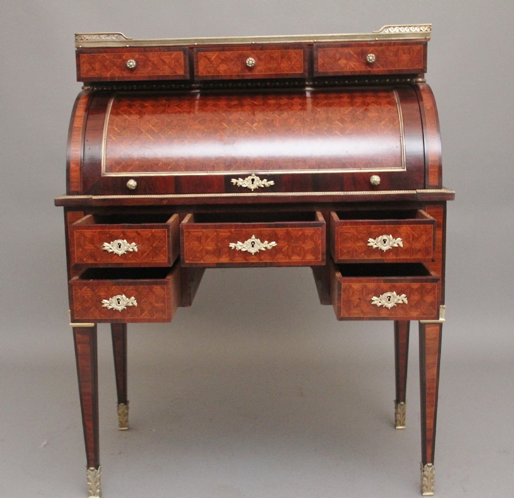 A 19th-century French kingwood cylinder desk featuring parquetry veneering, gilt-brass mounts, tapered square legs, and a curved roll-top section over multiple small drawers. View VI