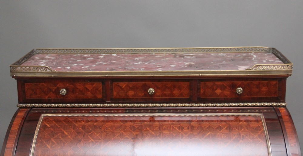 A 19th-century French kingwood cylinder desk featuring parquetry veneering, gilt-brass mounts, tapered square legs, and a curved roll-top section over multiple small drawers. View VII