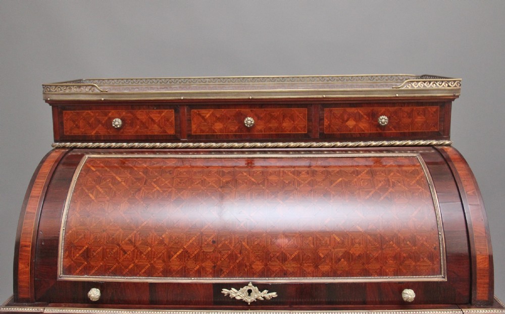 A 19th-century French kingwood cylinder desk featuring parquetry veneering, gilt-brass mounts, tapered square legs, and a curved roll-top section over multiple small drawers. View IX