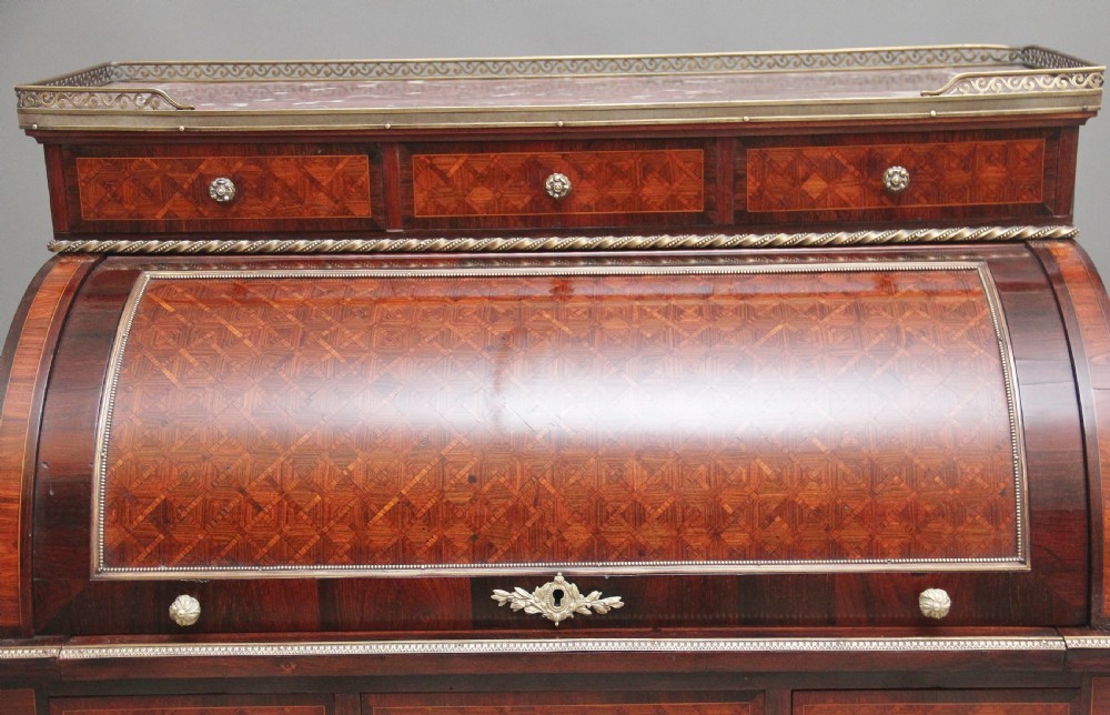 A 19th-century French kingwood cylinder desk featuring parquetry veneering, gilt-brass mounts, tapered square legs, and a curved roll-top section over multiple small drawers. View X
