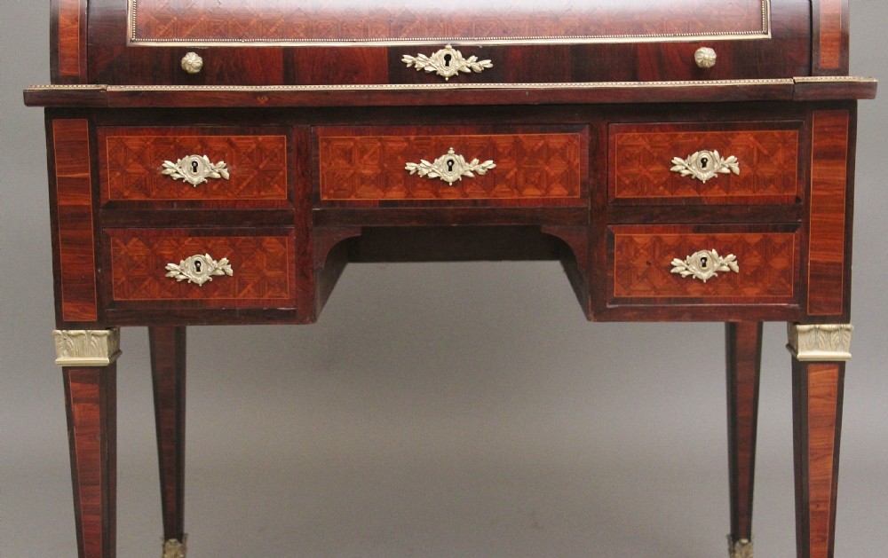 A 19th-century French kingwood cylinder desk featuring parquetry veneering, gilt-brass mounts, tapered square legs, and a curved roll-top section over multiple small drawers. View XIII