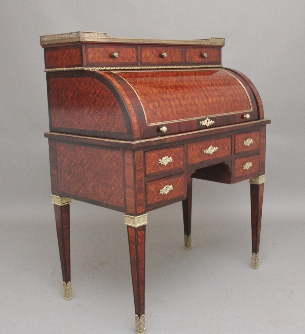 A 19th-century French kingwood cylinder desk featuring parquetry veneering, gilt-brass mounts, tapered square legs, and a curved roll-top section over multiple small drawers. View XVI