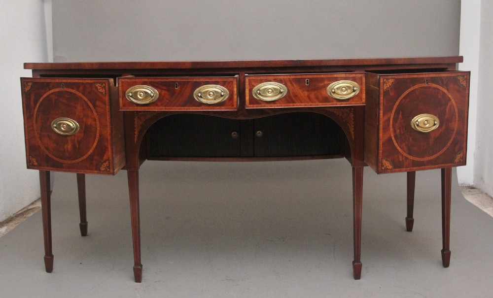 A 19th-century mahogany bowfront sideboard featuring marquetry inlay borders, brass oval handles, central arched drawer, and tapered legs. View II