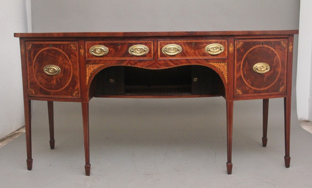 A 19th-century mahogany bowfront sideboard featuring marquetry inlay borders, brass oval handles, central arched drawer, and tapered legs. View III