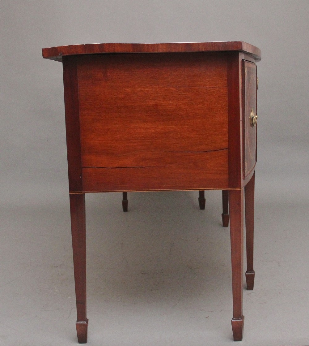 A 19th-century mahogany bowfront sideboard featuring marquetry inlay borders, brass oval handles, central arched drawer, and tapered legs. View V