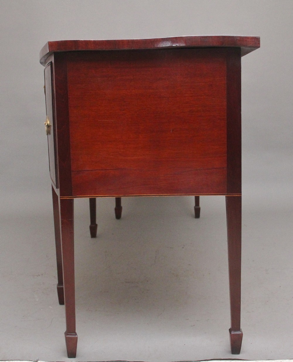 A 19th-century mahogany bowfront sideboard featuring marquetry inlay borders, brass oval handles, central arched drawer, and tapered legs. View VII