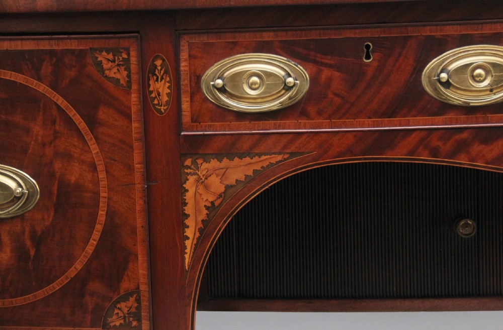 A 19th-century mahogany bowfront sideboard featuring marquetry inlay borders, brass oval handles, central arched drawer, and tapered legs. View VIII