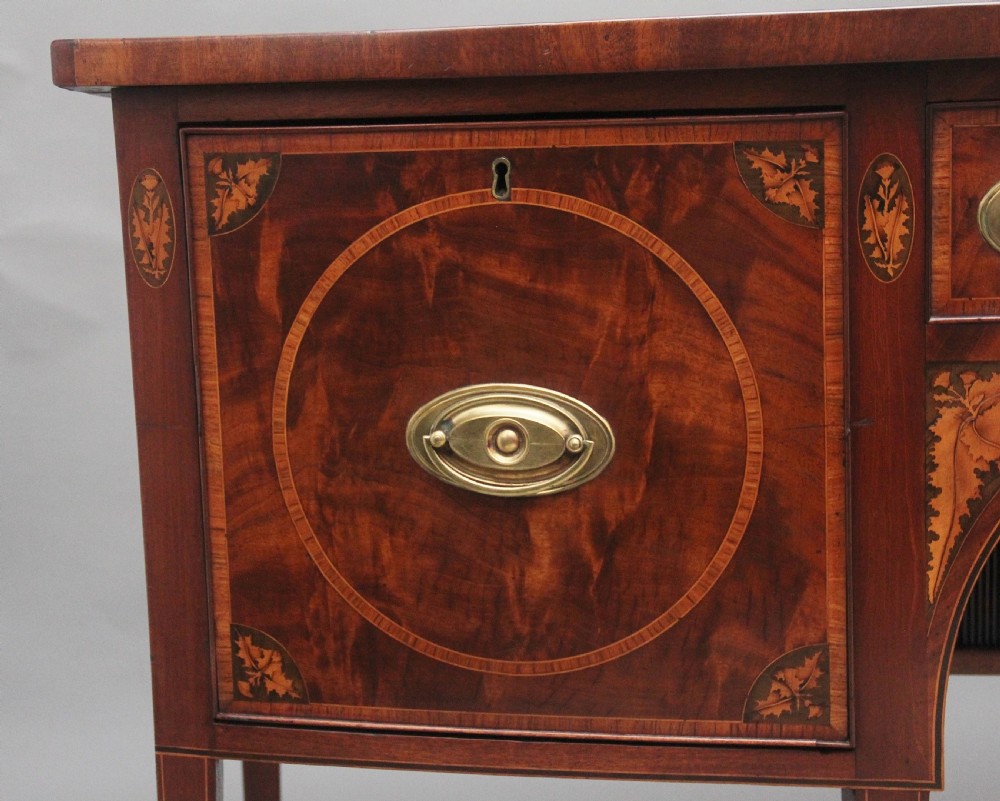 A 19th-century mahogany bowfront sideboard featuring marquetry inlay borders, brass oval handles, central arched drawer, and tapered legs. View IX
