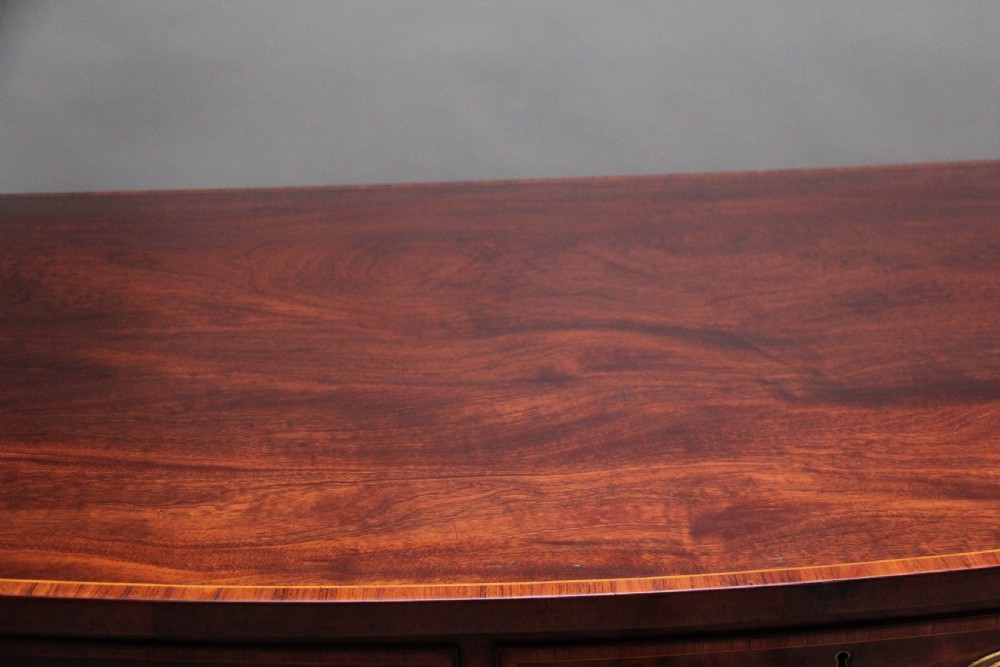 A 19th-century mahogany bowfront sideboard featuring marquetry inlay borders, brass oval handles, central arched drawer, and tapered legs. View XI