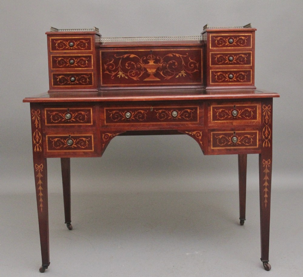 A 19th-century mahogany writing desk featuring intricate floral marquetry inlays, a raised gallery with drawers, square tapered legs, and brass castors.