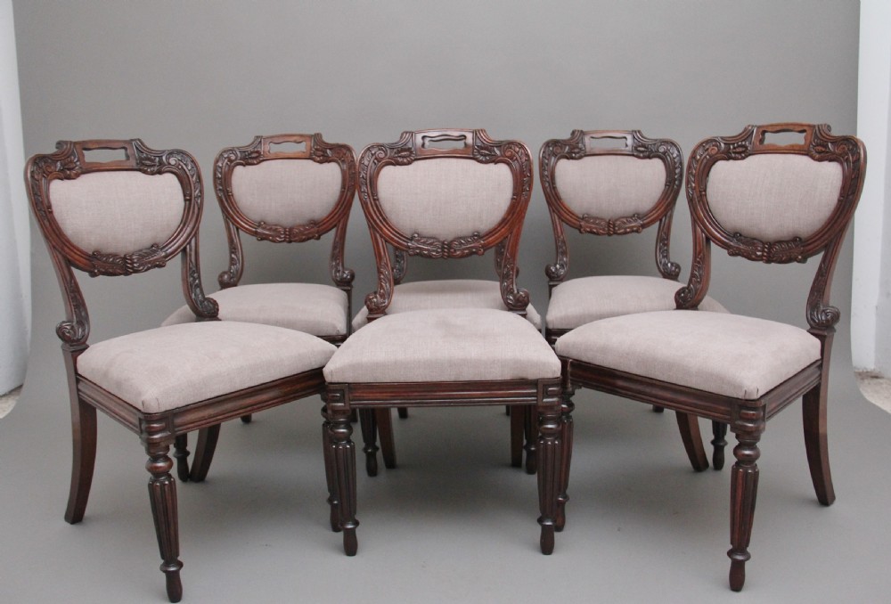 A set of six carved dark rosewood dining chairs with neutral fabric upholstered seats and padded backs.