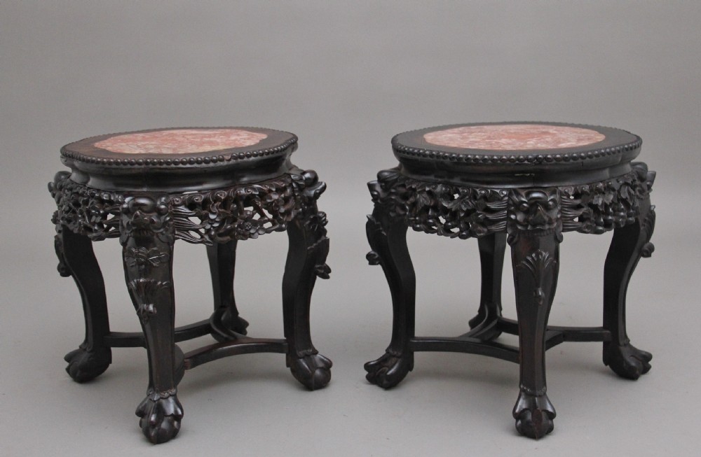 A pair of 19th-century Chinese dark hardwood low stands featuring carved pierced aprons, cabriole legs with claw feet, and round pink marble tops. View II