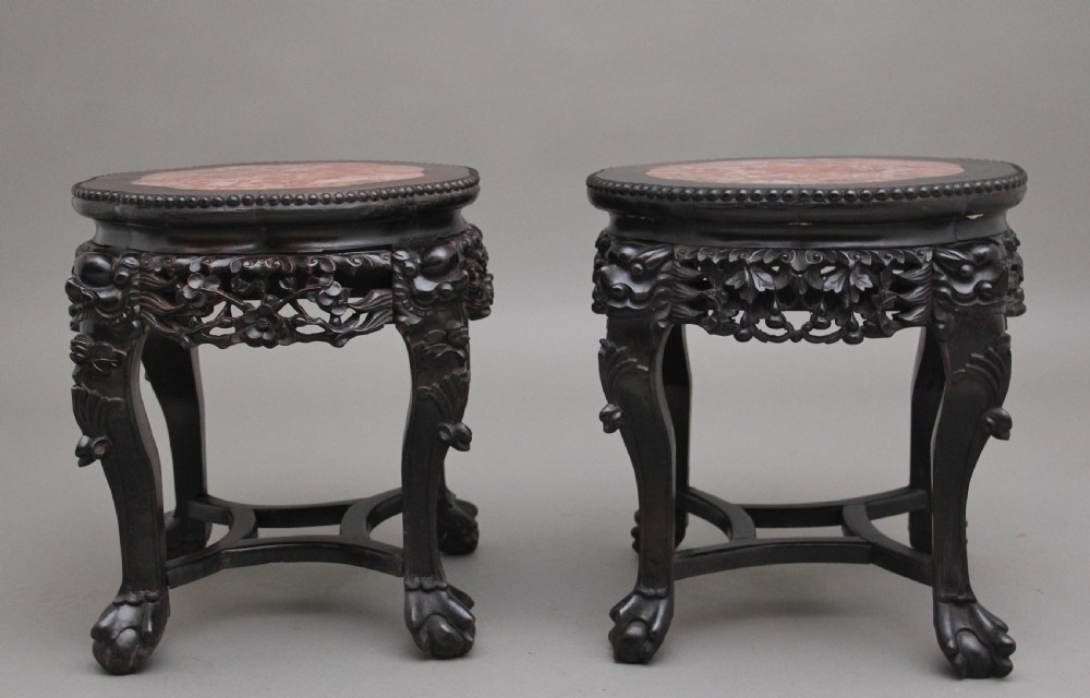 A pair of 19th-century Chinese dark hardwood low stands featuring carved pierced aprons, cabriole legs with claw feet, and round pink marble tops. View V