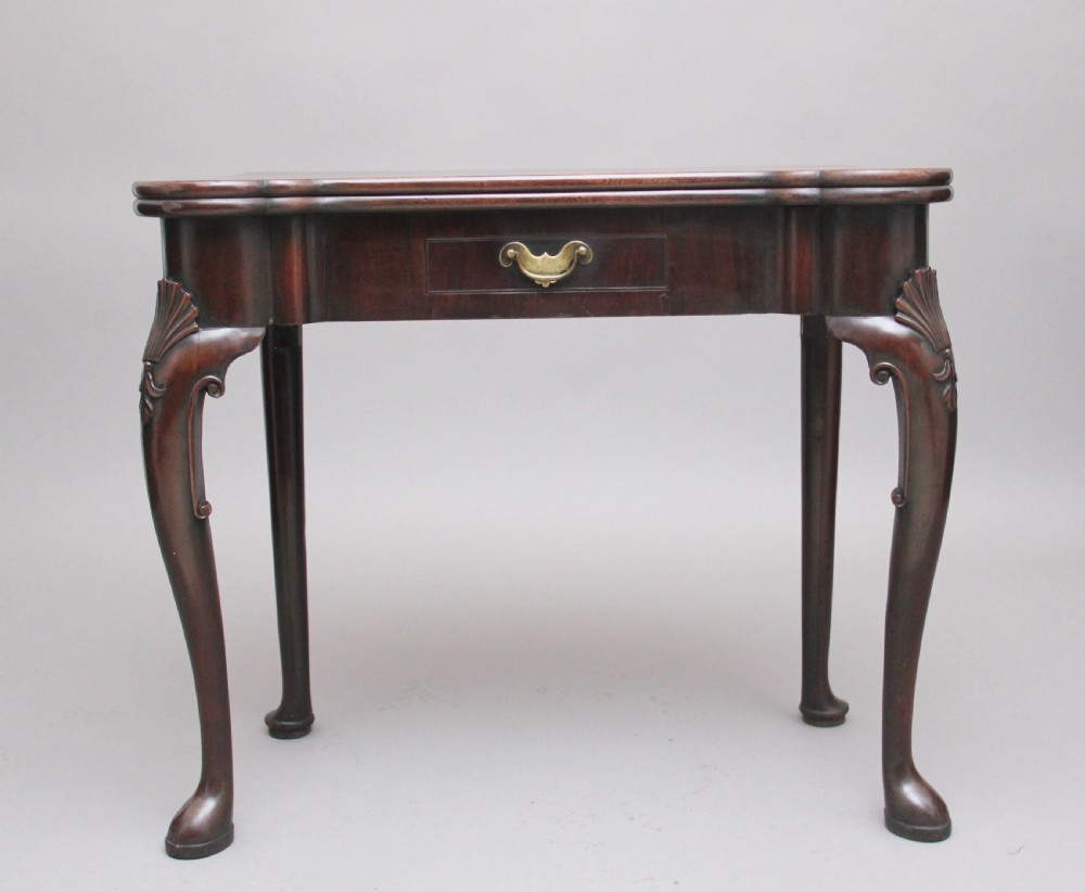 An 18th-century dark mahogany games table with a fold-over top, shell-carved cabriole legs, pad feet, and a central drawer.