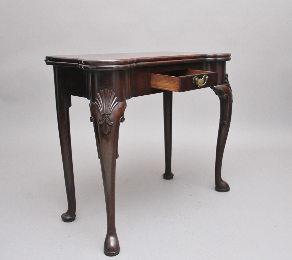 An 18th-century dark mahogany games table with a fold-over top, shell-carved cabriole legs, pad feet, and a central drawer. View V