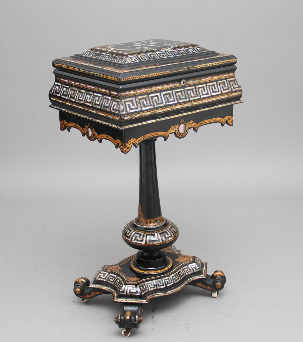 A nineteenth-century black lacquered papier-mache work table featuring mother-of-pearl Greek key inlay, hand-gilded detailing, a hinged box top, and a pedestal base on castors.