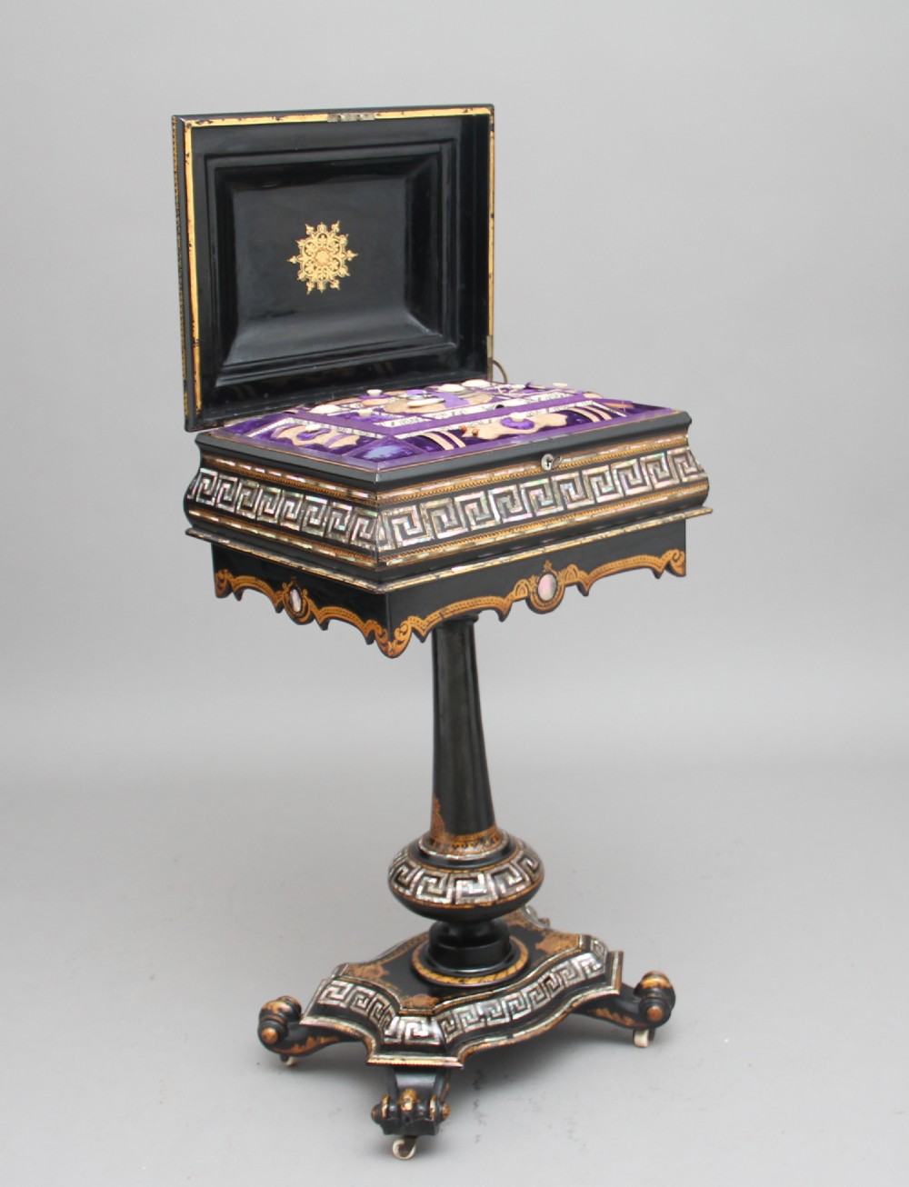 A nineteenth-century black lacquered papier-mache work table featuring mother-of-pearl Greek key inlay, hand-gilded detailing, a hinged box top, and a pedestal base on castors. View II