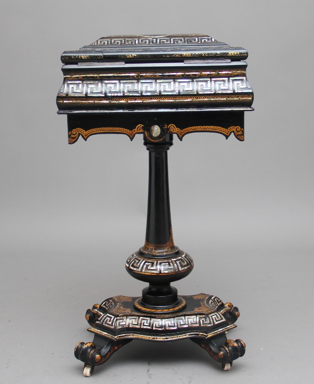 A nineteenth-century black lacquered papier-mache work table featuring mother-of-pearl Greek key inlay, hand-gilded detailing, a hinged box top, and a pedestal base on castors. View V