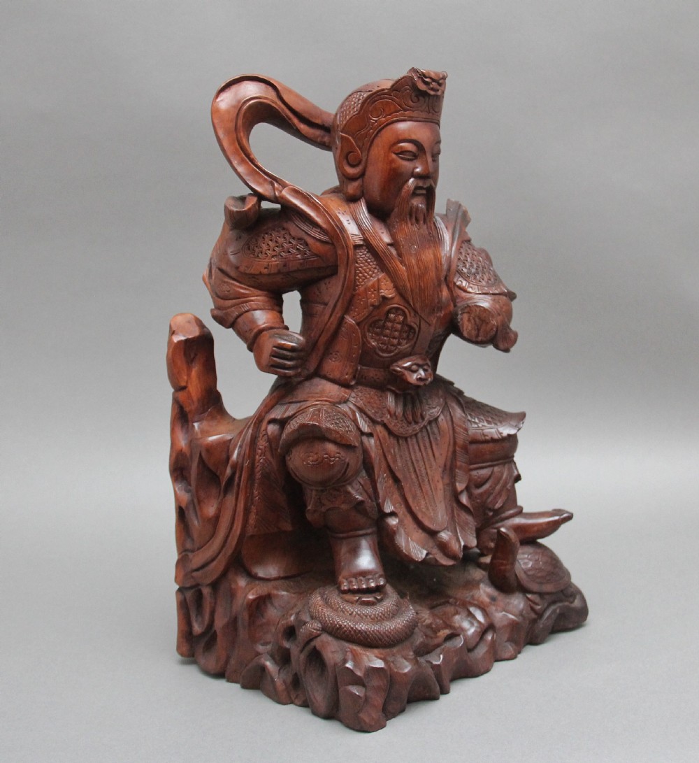 A 19th-century Chinese hand-carved wooden figure depicting a bearded warrior deity in armour standing over a serpent and tortoise.