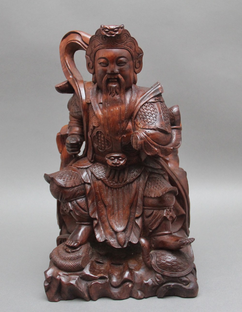 A 19th-century Chinese hand-carved wooden figure depicting a bearded warrior deity in armour standing over a serpent and tortoise. View II
