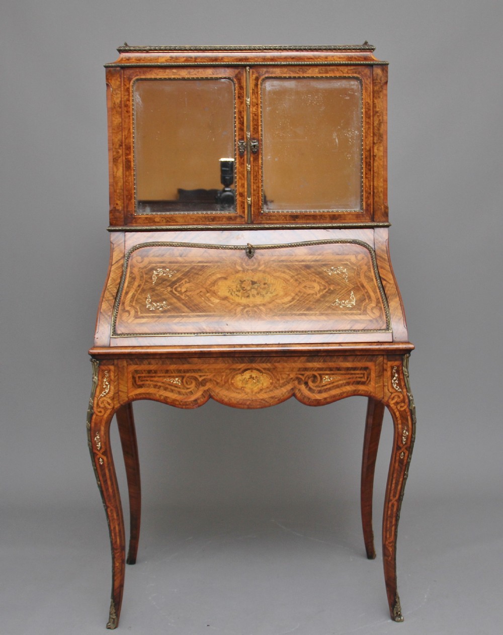 A nineteenth-century French walnut and kingwood bureau de dame with floral marquetry inlay, brass mounts, cabriole legs, and an upper cabinet with mirrored doors. View X