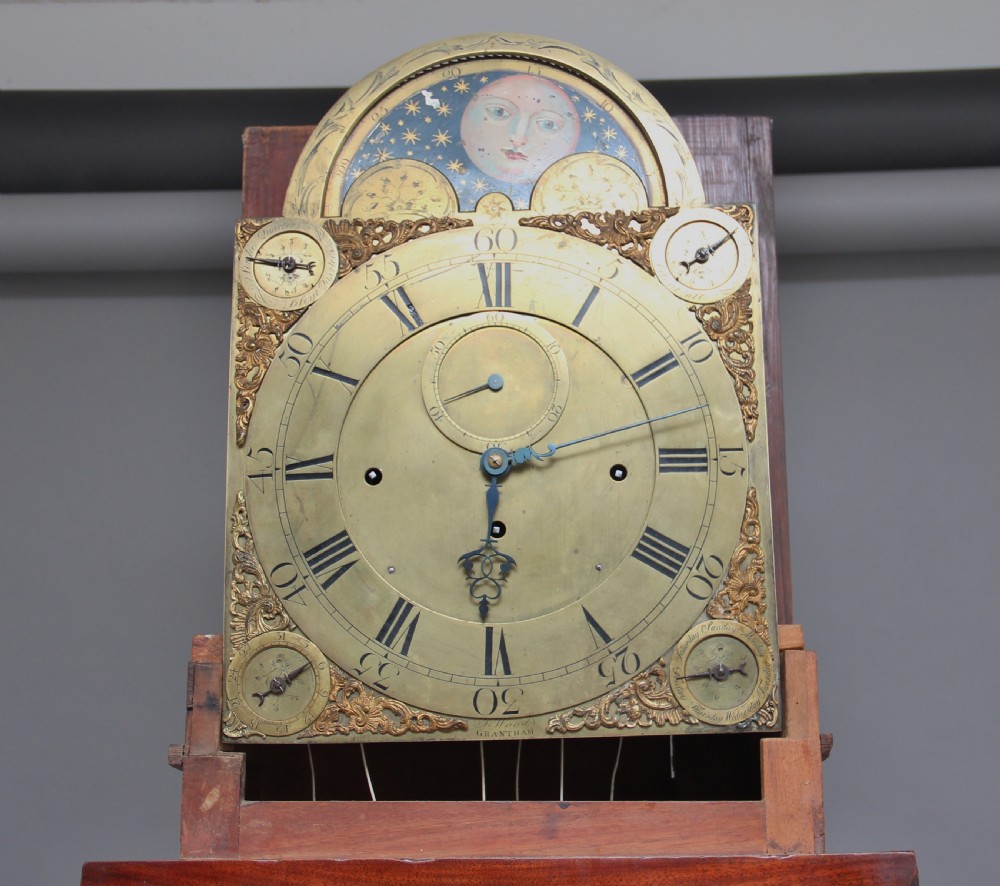 An 18th-century Georgian flame mahogany longcase clock featuring an arched hood, brass dial with moon phase display, and polished wood casing. View V