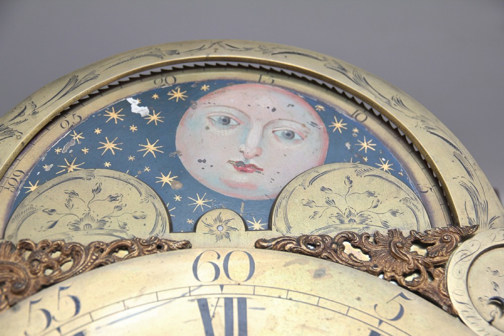 An 18th-century Georgian flame mahogany longcase clock featuring an arched hood, brass dial with moon phase display, and polished wood casing. View VI