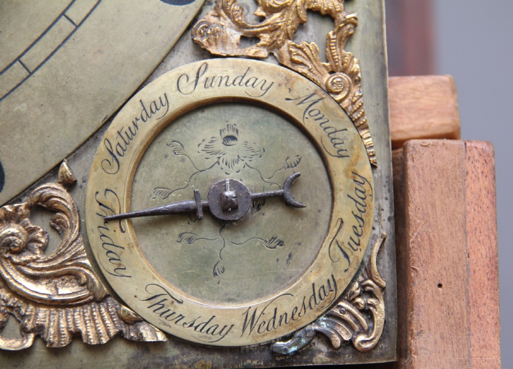 An 18th-century Georgian flame mahogany longcase clock featuring an arched hood, brass dial with moon phase display, and polished wood casing. View VII