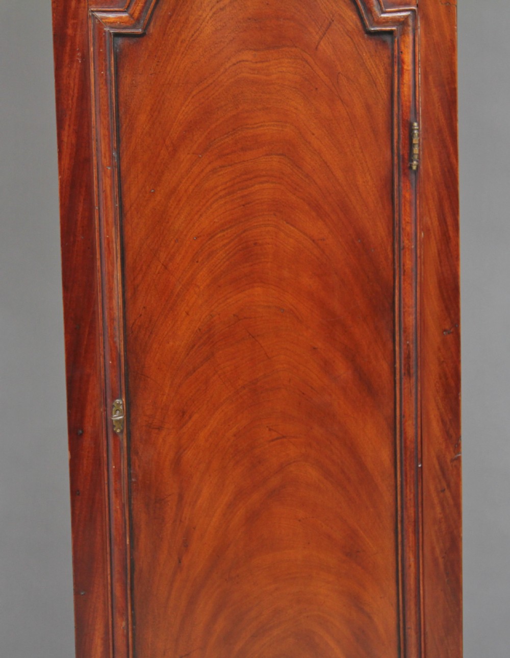 An 18th-century Georgian flame mahogany longcase clock featuring an arched hood, brass dial with moon phase display, and polished wood casing. View XIV